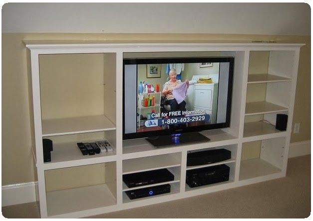 White built-in entertainment center with TV, shelves, and black media devices in a living room