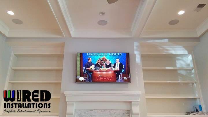 Living room with built-in white shelves framing a TV above a fireplace, and a Wired Installs logo at left.