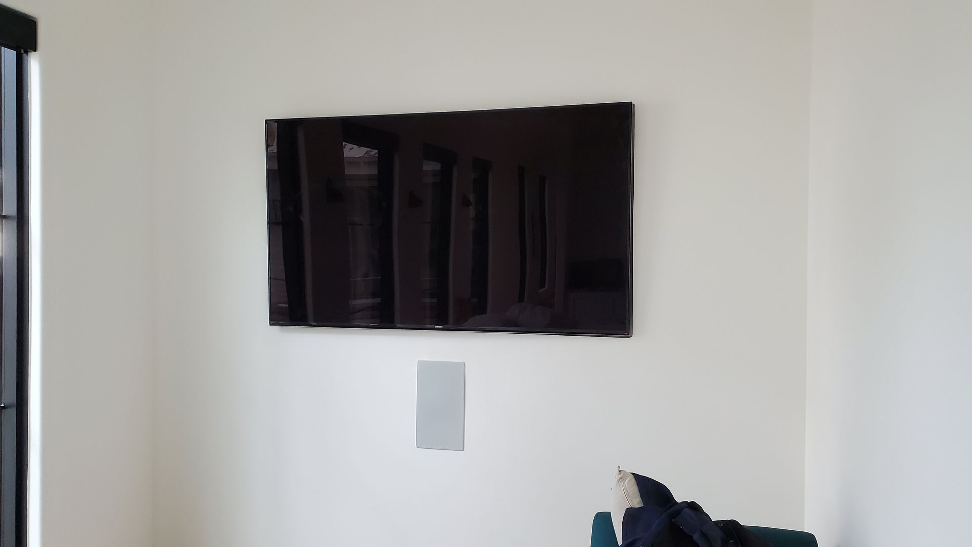Wall-mounted flat-screen TV on a white wall with a small gray panel below it.