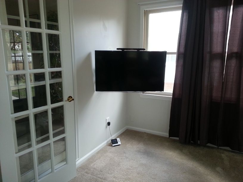 Small room with wall-mounted TV, glass door, carpet, and dark curtains by a window.