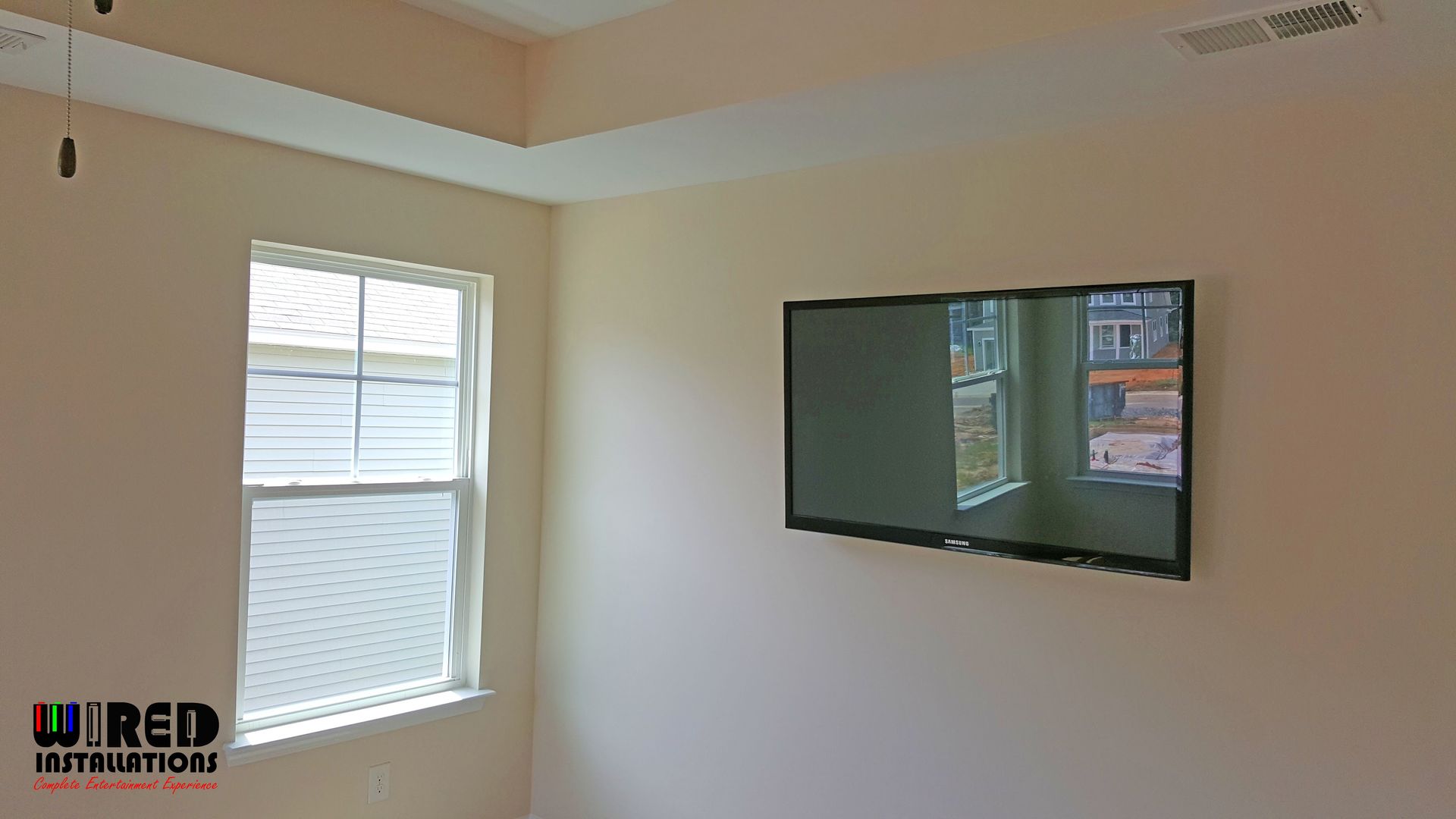 Empty beige room with a window and a wall-mounted TV displaying a bright outdoor scene