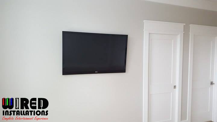Wall-mounted black TV on a white wall beside a white door, with a JRED Installations logo in the corner