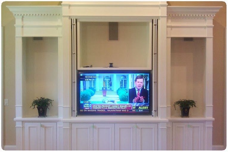 White built-in entertainment wall with a TV, flanked by niches with small potted plants.