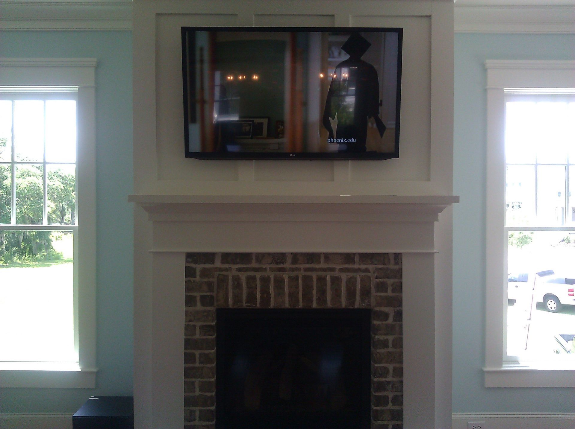 Living room fireplace with a wall-mounted TV above it, flanked by two bright windows.