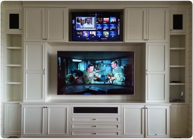 Built-in wall unit with two TVs, white cabinets, and drawers in a living room