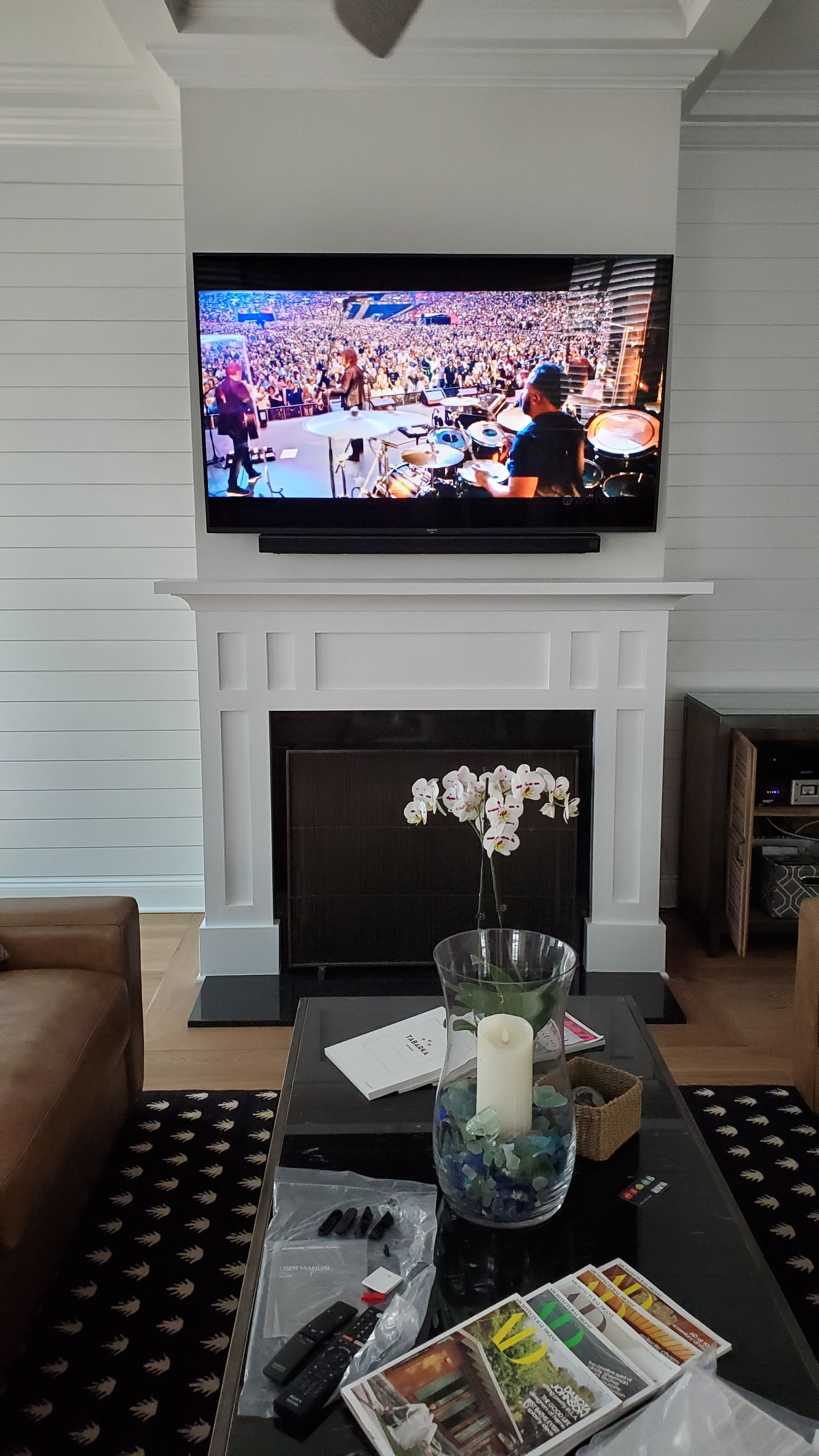 Living room with a TV above a white fireplace and a glass coffee table in the foreground