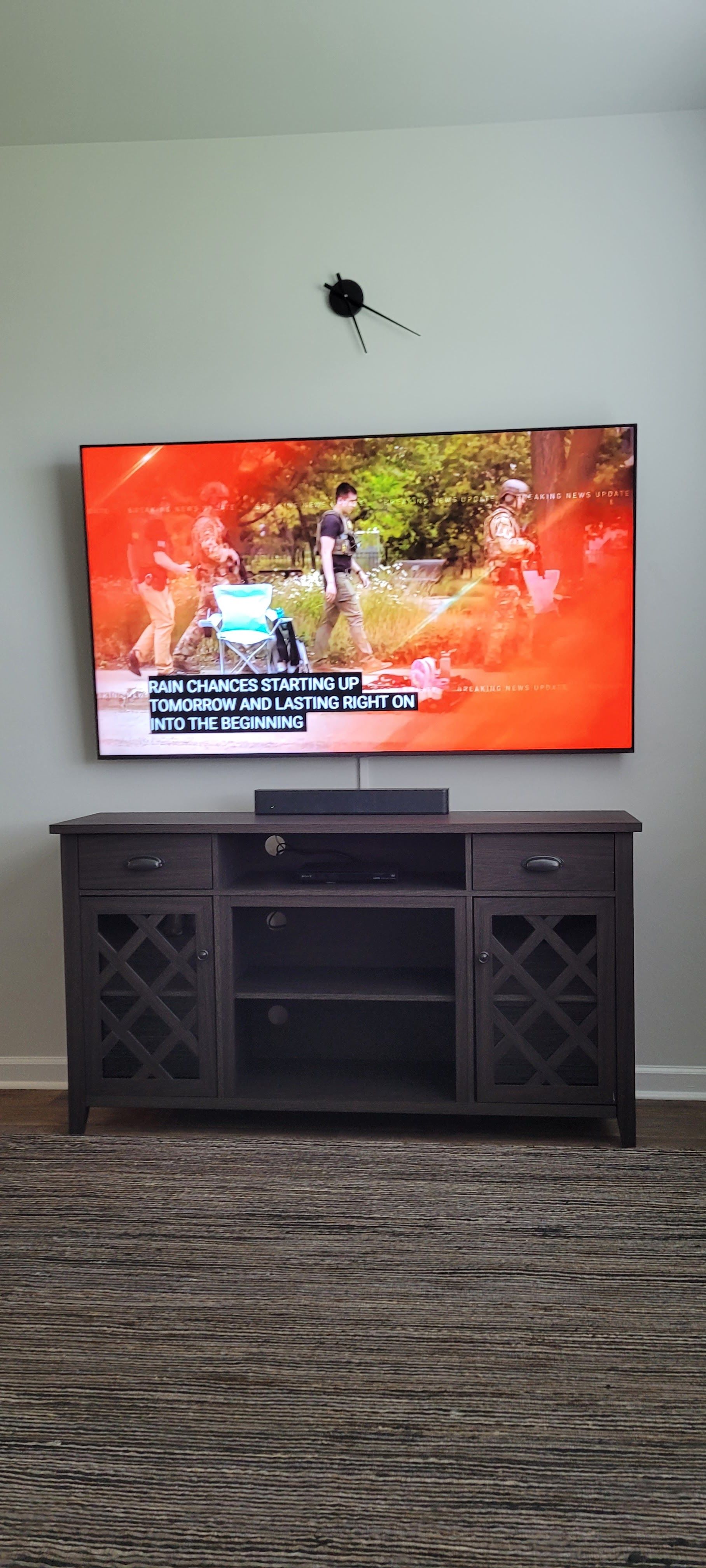 Living room with a wall-mounted TV above a dark media console on a patterned carpet.