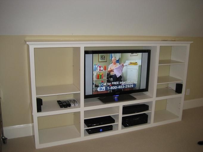 White built-in wall unit with a TV in the center, shelves, and electronics in a living room.