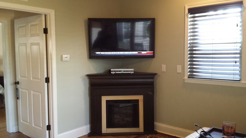 Living room with wall-mounted TV above a black fireplace, beige walls, and a window with blinds.