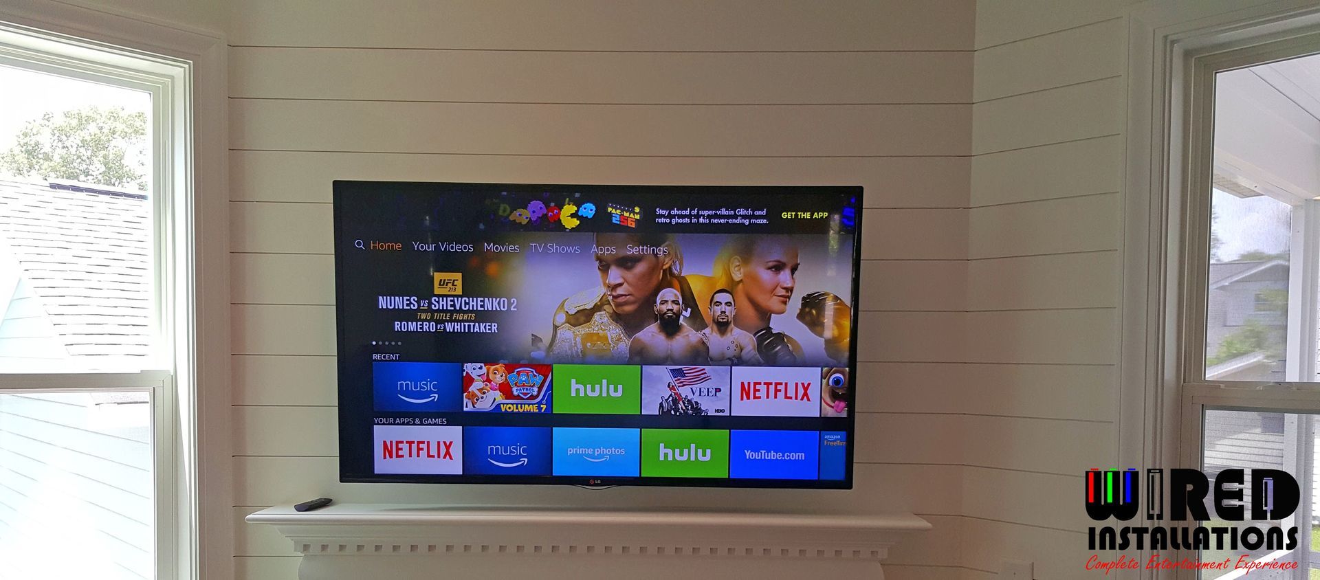 Living room wall with a mounted TV showing a colorful streaming home screen between two windows