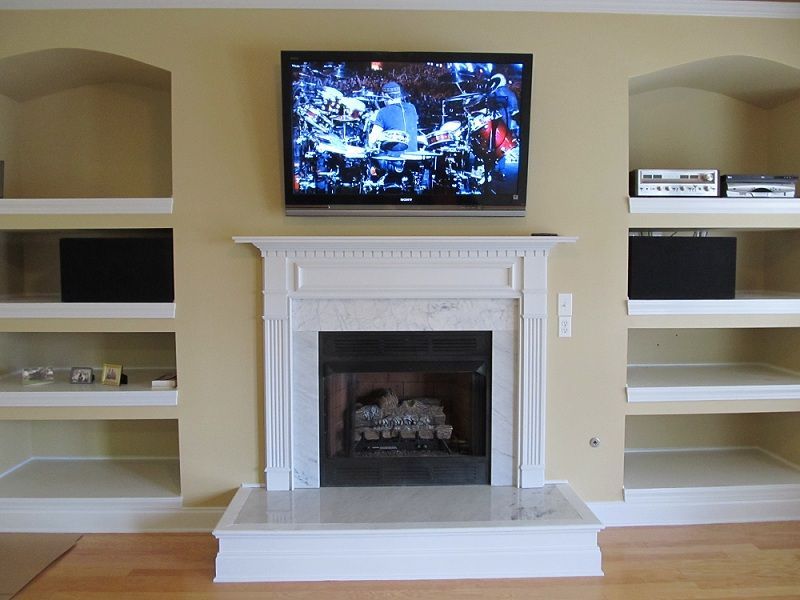 Living room with white fireplace, wall-mounted TV, and built-in shelves on both sides