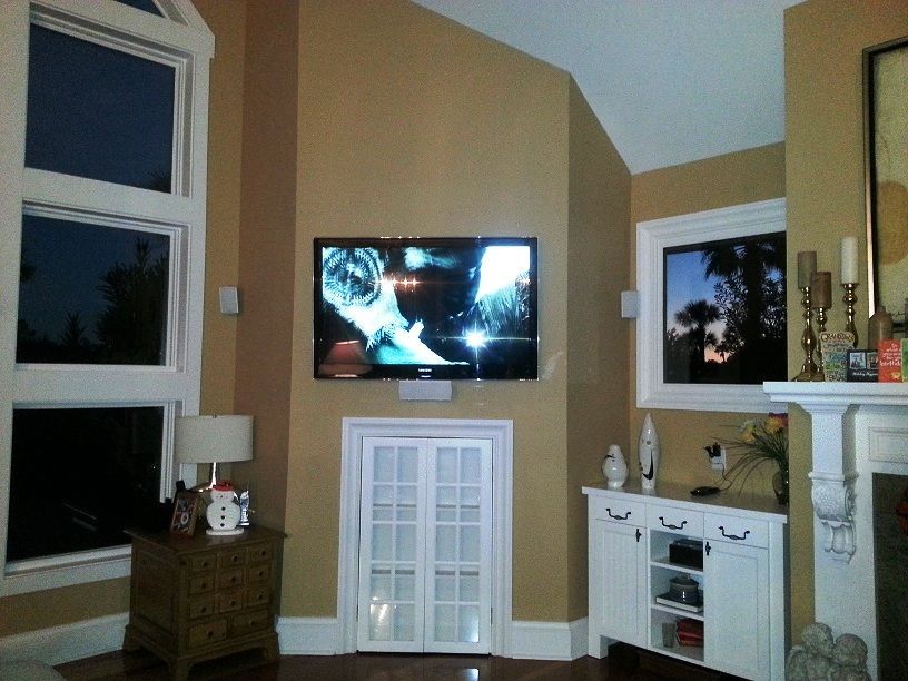 Living room with wall-mounted TV above white cabinet, tan walls, and a fireplace on the right.