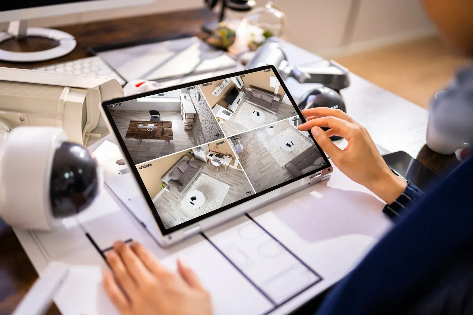 Person using a tablet to view home security camera feeds at a desk