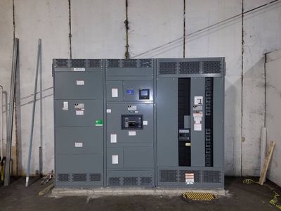 Large gray industrial generator/control unit against a concrete wall in a utility room