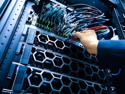 Hand adjusting cables in a server rack with lit network equipment and hexagonal cooling fans