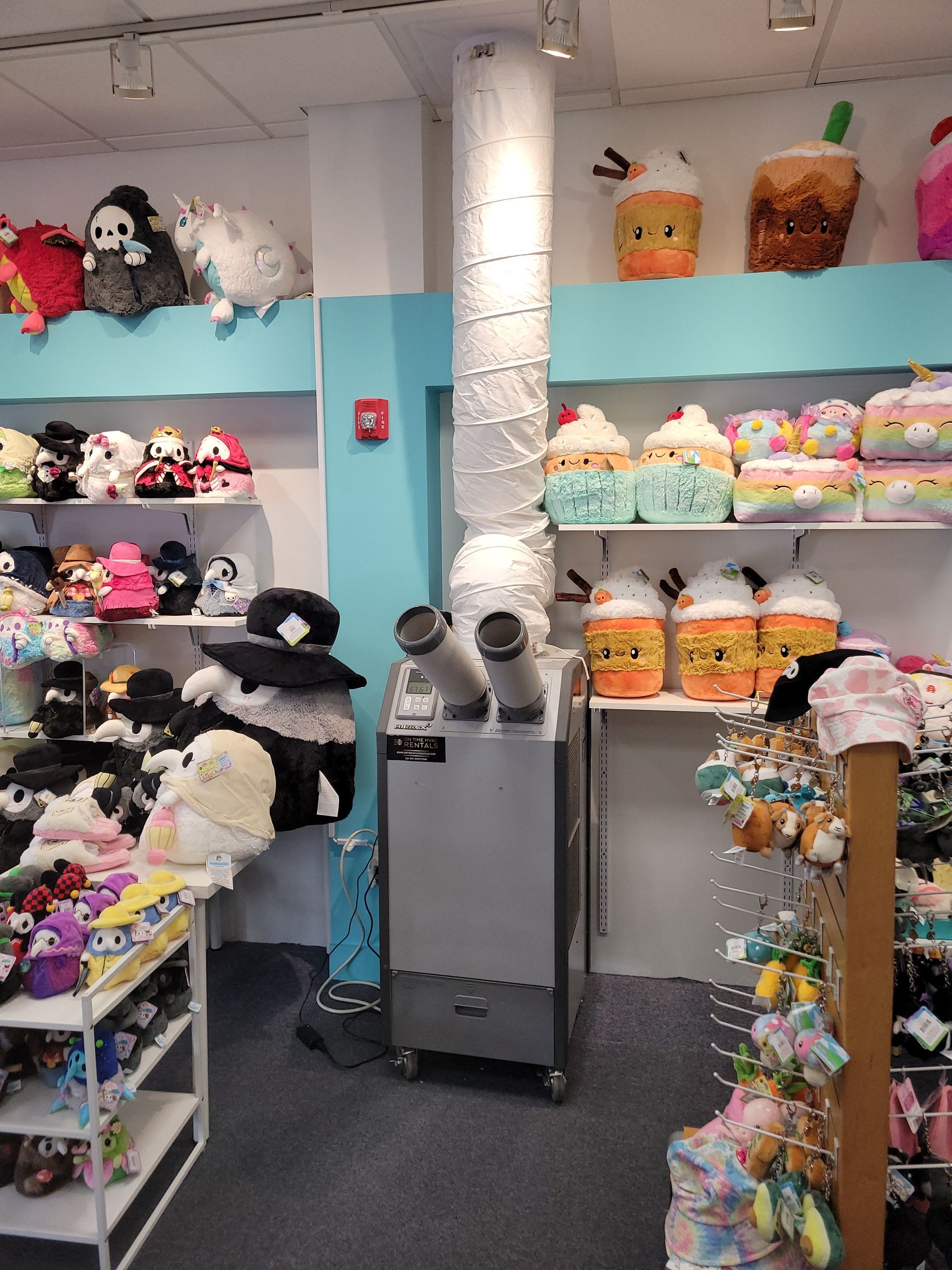 Shelves filled with various plush toys in a retail store, with a portable air conditioner and vent hose in the center.
