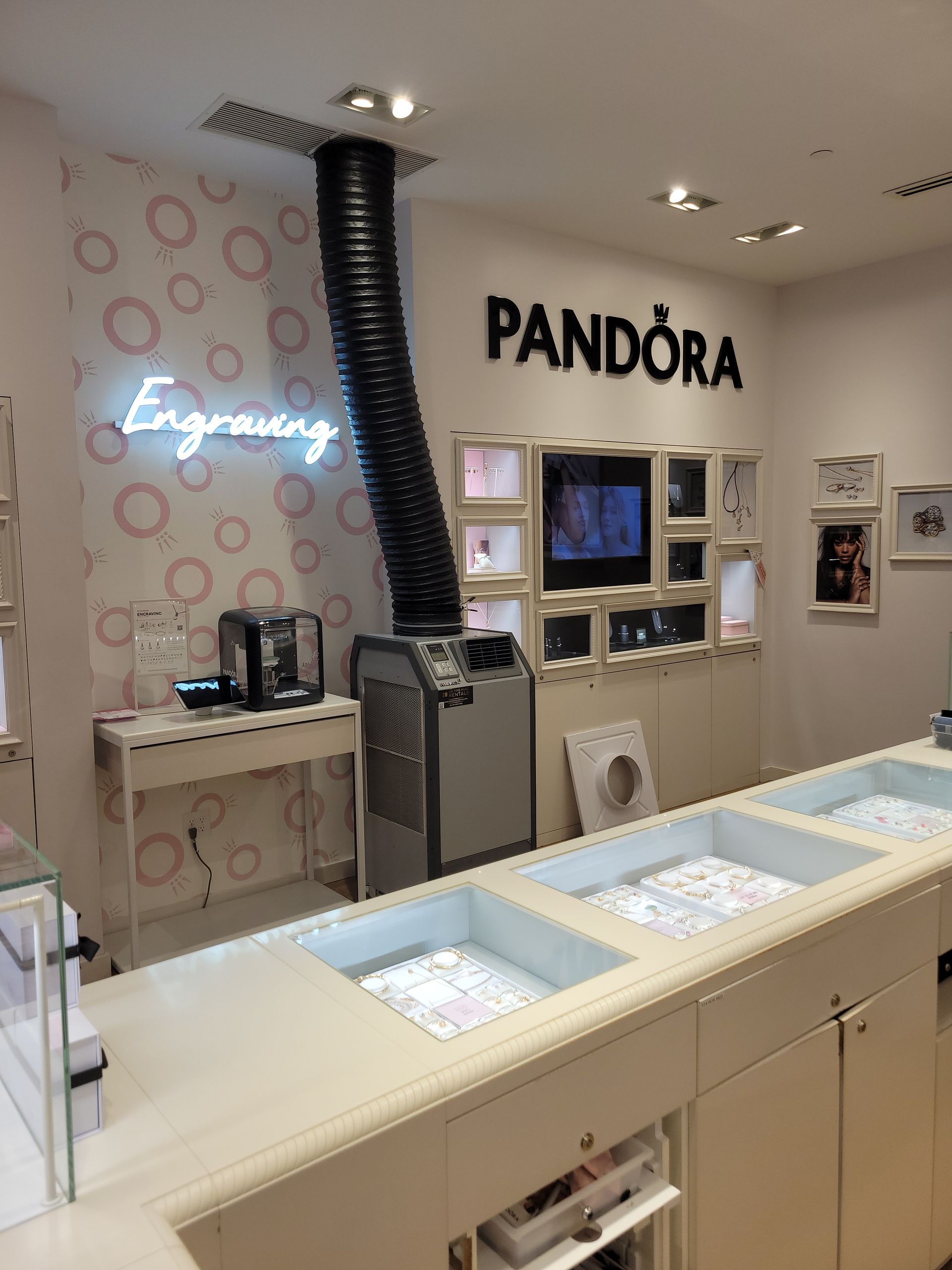 Interior of a Pandora jewelry store featuring an engraving station with a large exhaust tube and glass display counters.