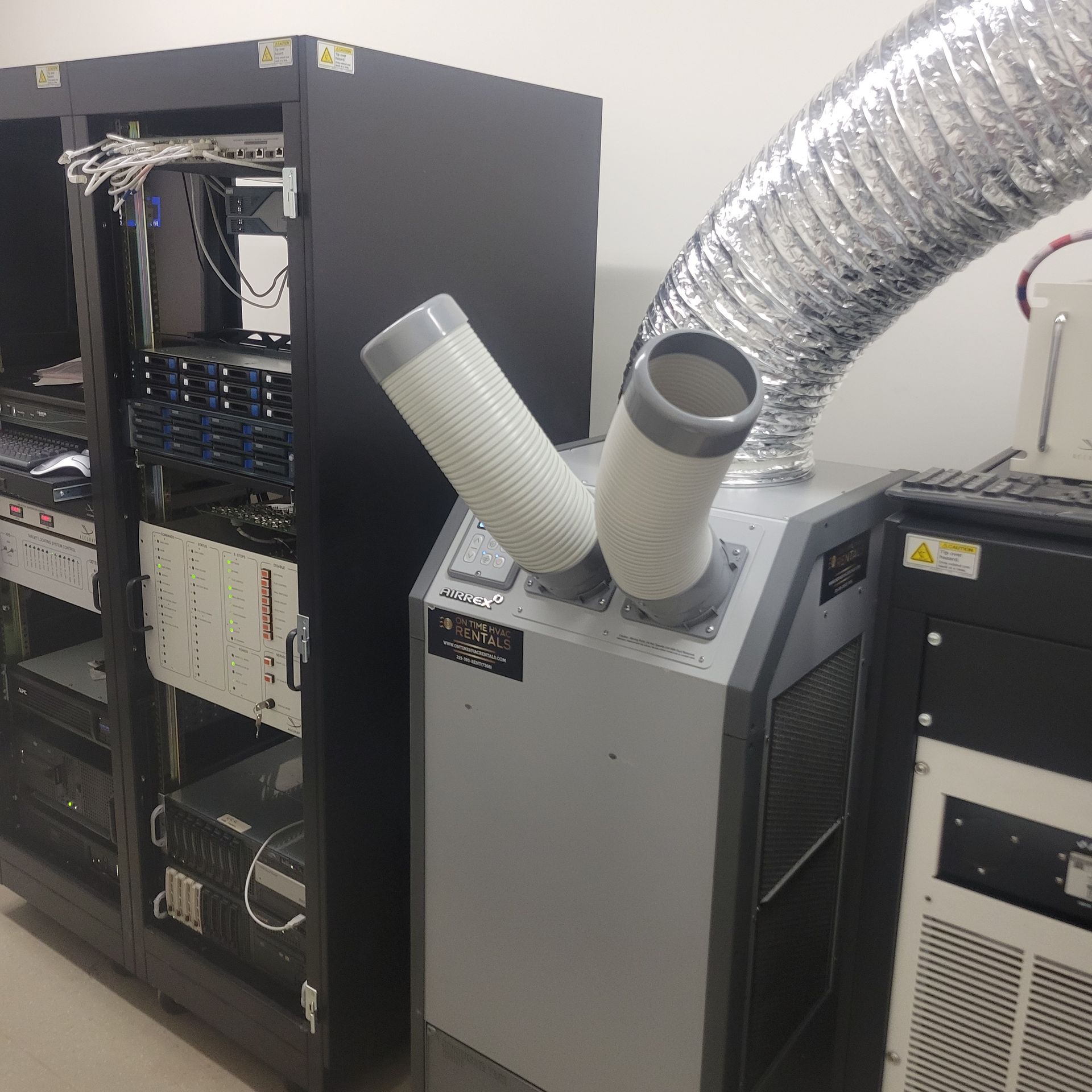 A portable air conditioning unit with two output ducts positioned next to a black server rack filled with equipment.