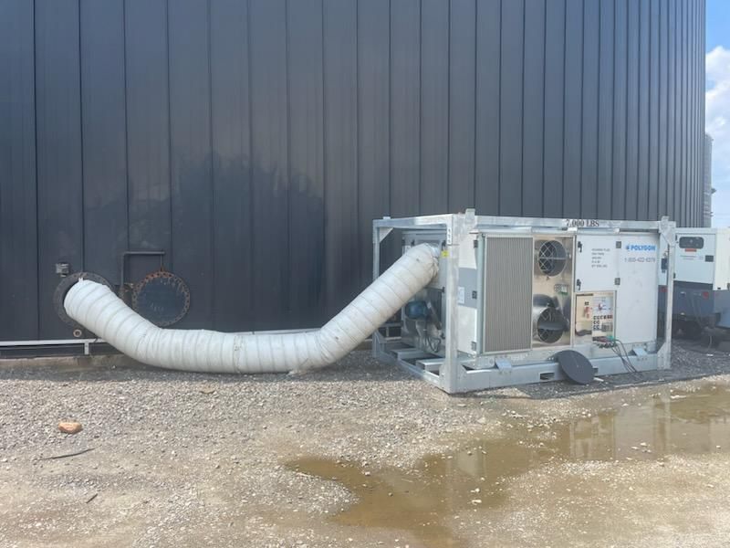 A portable industrial cooling unit connected by a large white flexible duct to a dark metal storage tank on gravel.