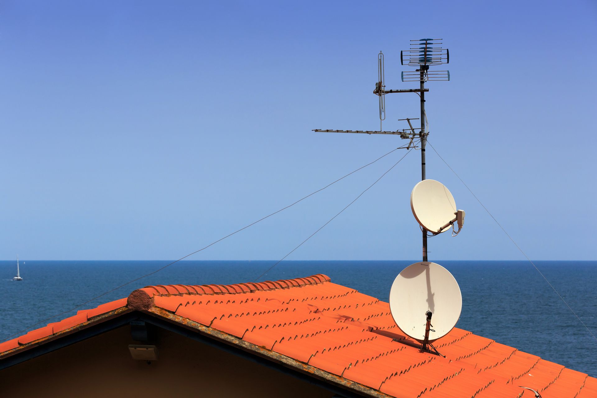 Antenna TV sul tetto e due parabole bianche affacciate sul mare blu