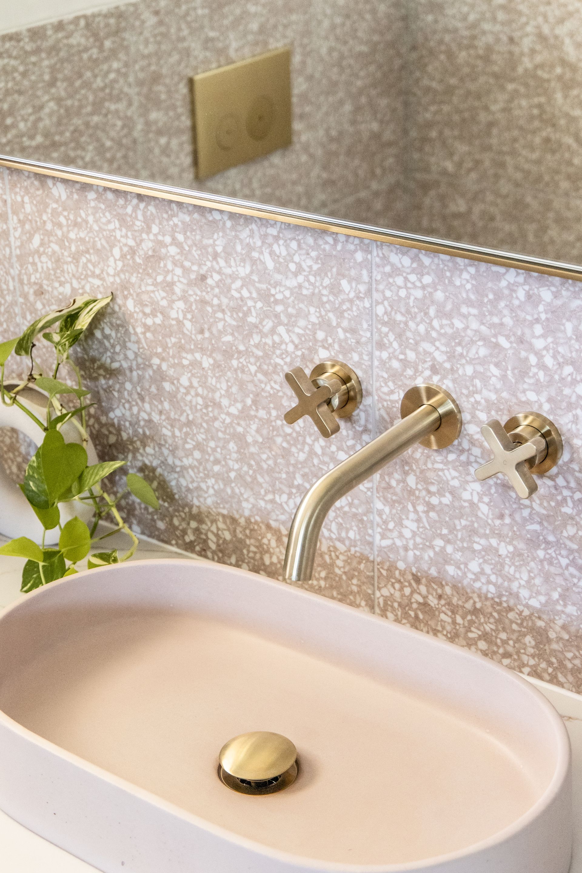 Pink oval sink with brass fixtures, against a speckled wall in a bathroom.