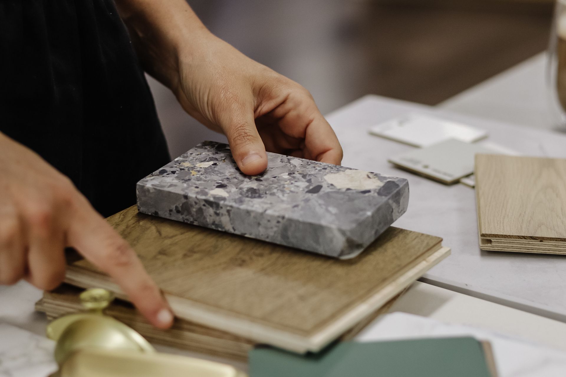 Hands comparing a stone sample to a wood plank, part of design materials.