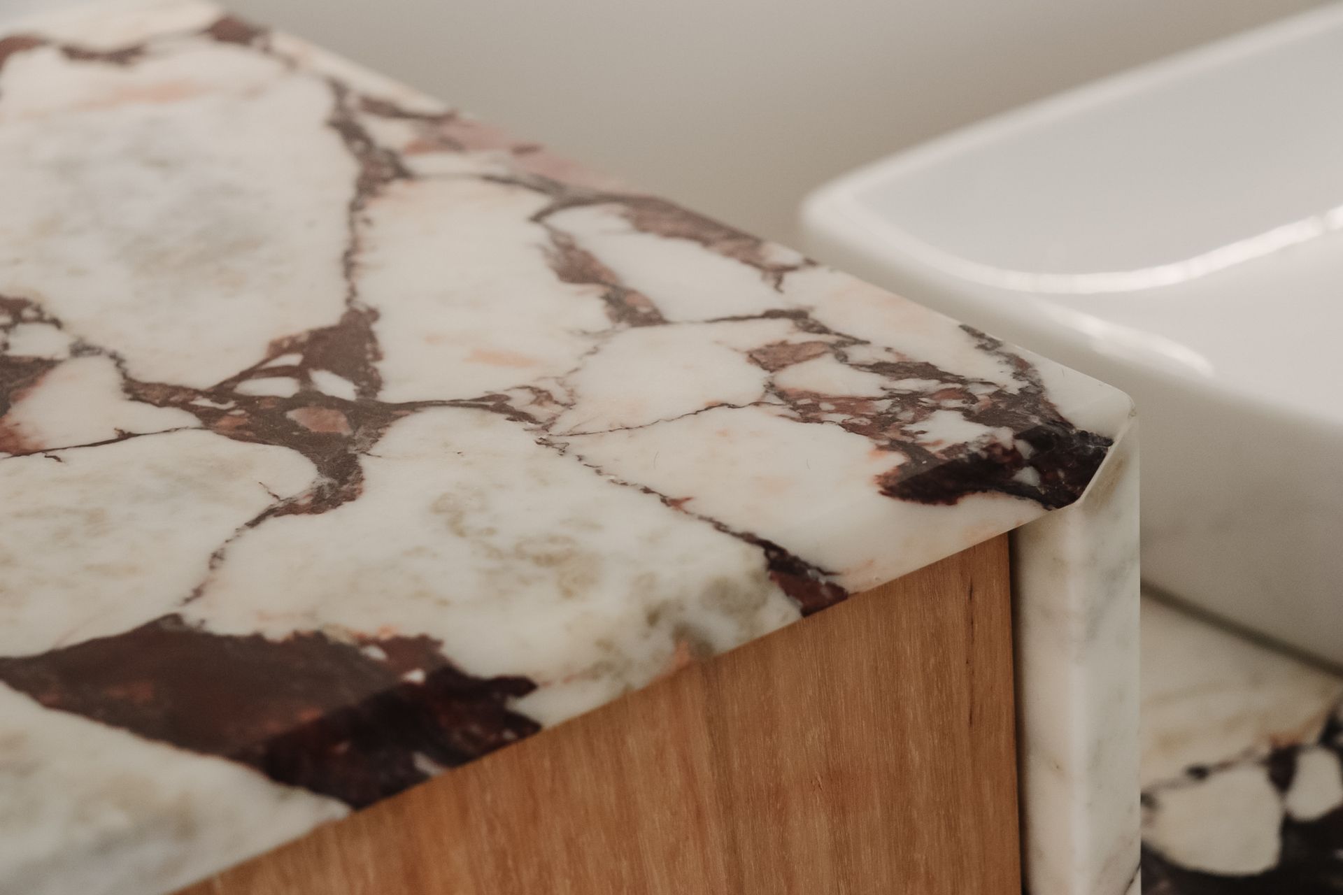 Close-up of a marble-patterned countertop edge with a wooden base, next to a white sink.