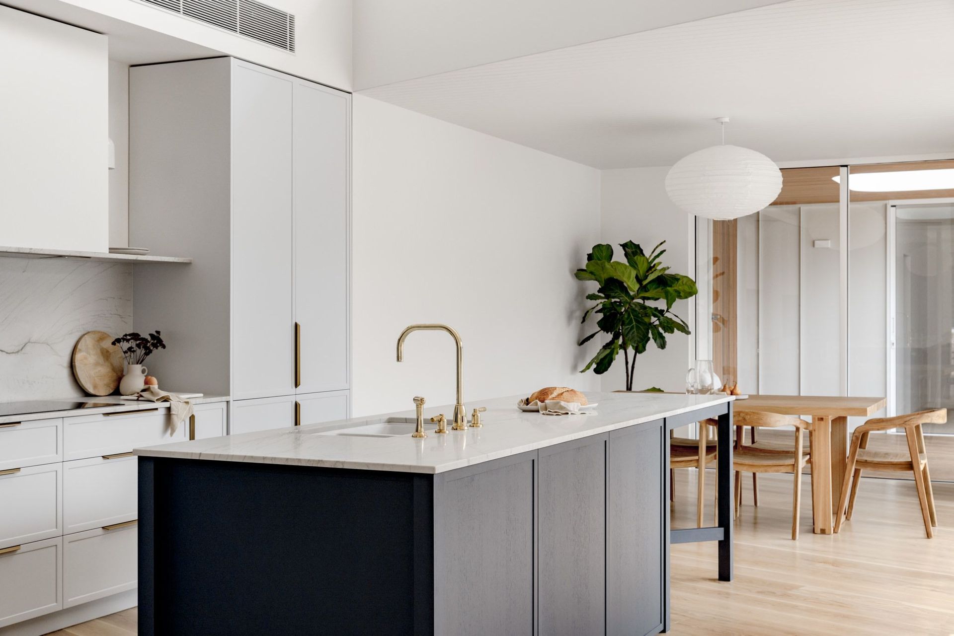 Modern kitchen with dark island, gold faucet, and light wood dining area.