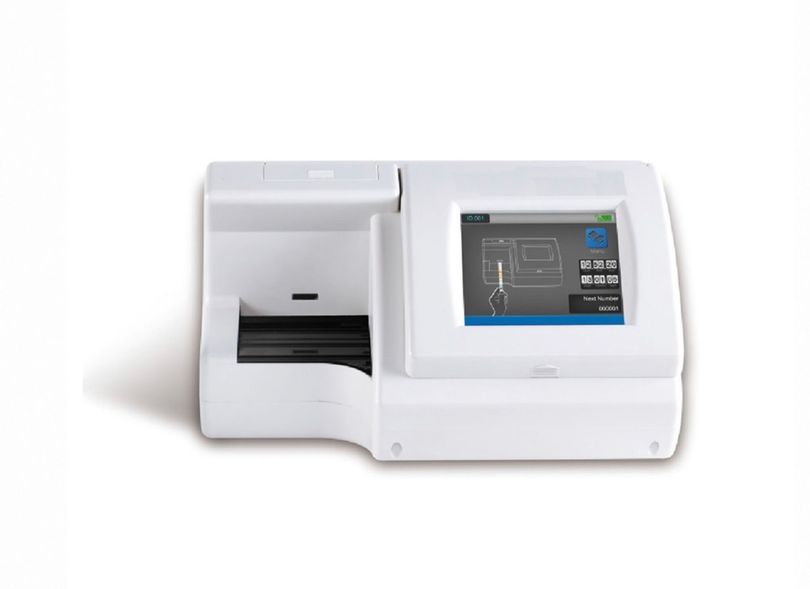Manos enguantadas colocando una tira reactiva en un analizador de laboratorio con pantalla digital.