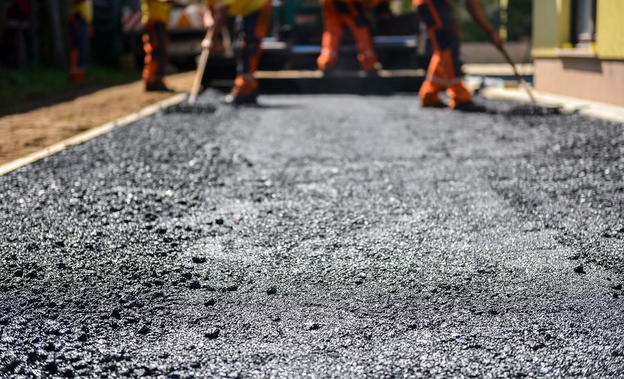Workers paving a driveway with dark asphalt.