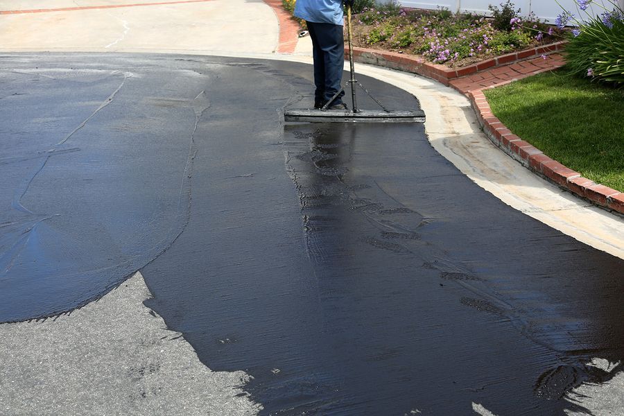 Person applying black sealant to asphalt driveway with a squeegee.