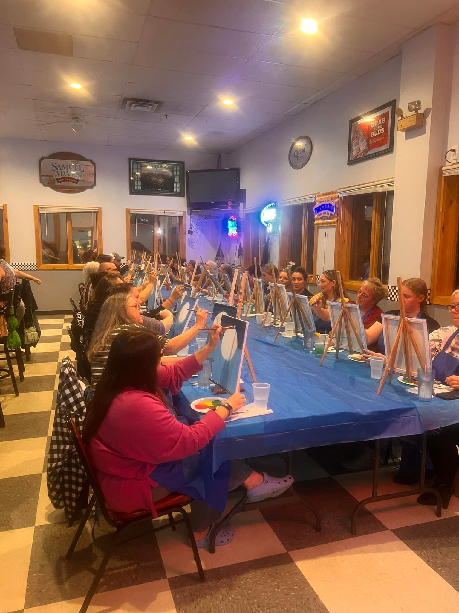 A group of people are sitting at tables in a room painting.