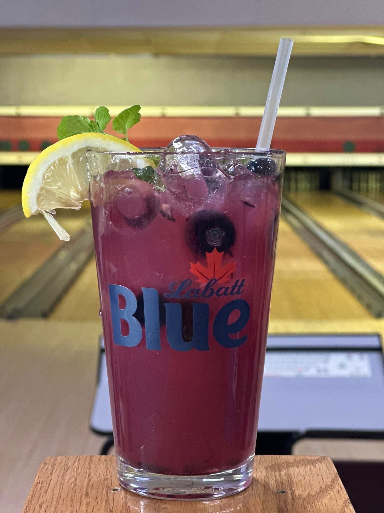 A glass of blueberry lemonade with ice and a straw in a bowling alley.