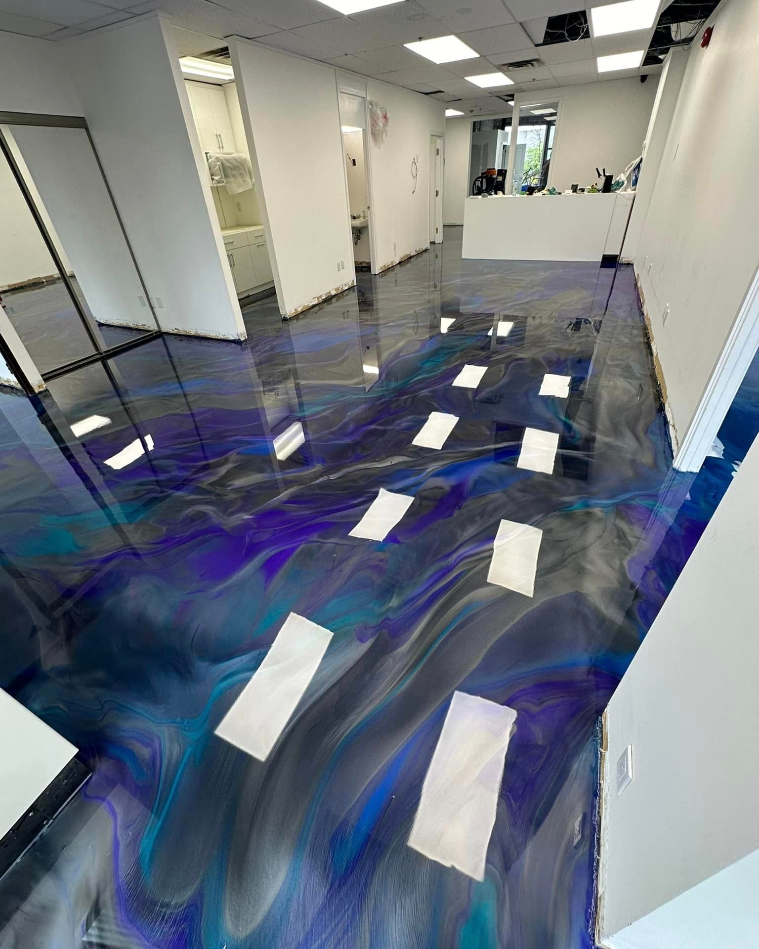 Hallway with glossy blue-purple floor coating and white taped rectangles under renovation