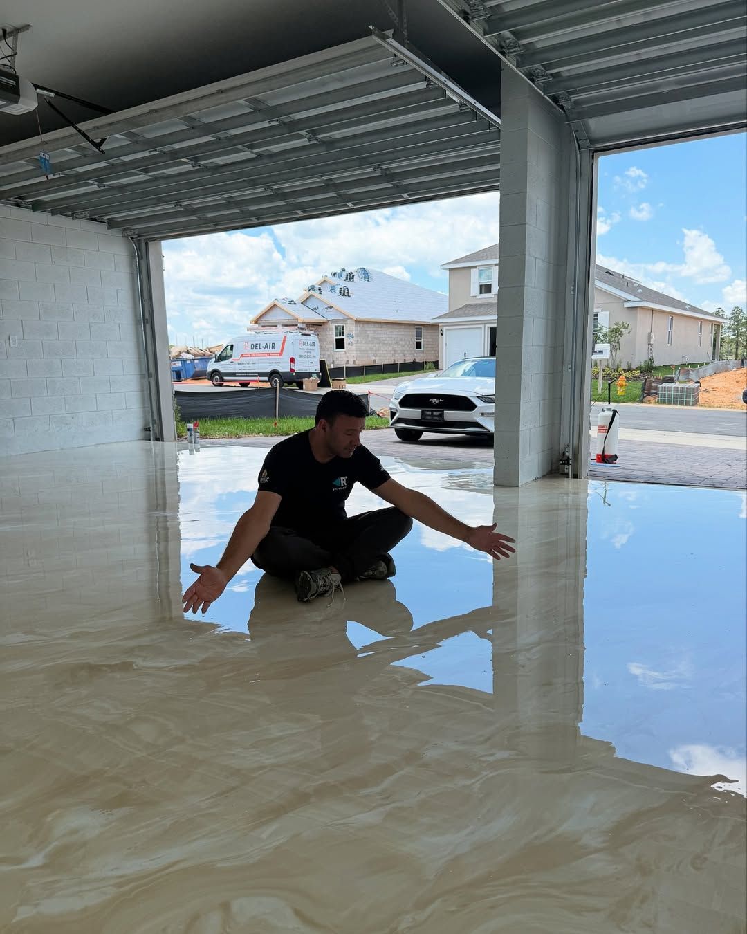 Person crouching in a flooded garage under a carport, with muddy water reflecting the street outside.