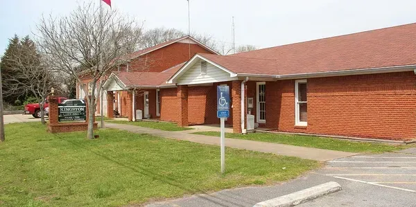 Red brick building with a covered entrance, blue accessibility sign, and parking lot in front