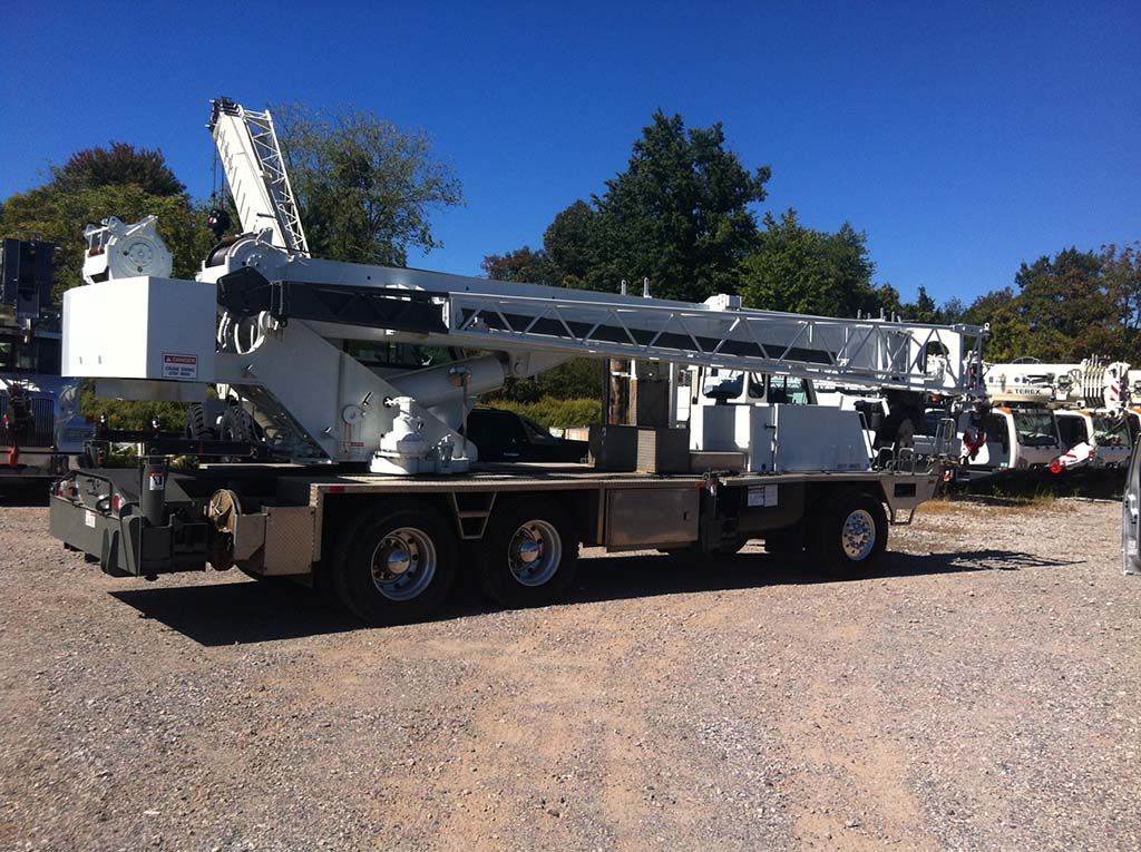 White crane truck with extended boom parked on gravel under a clear blue sky.
