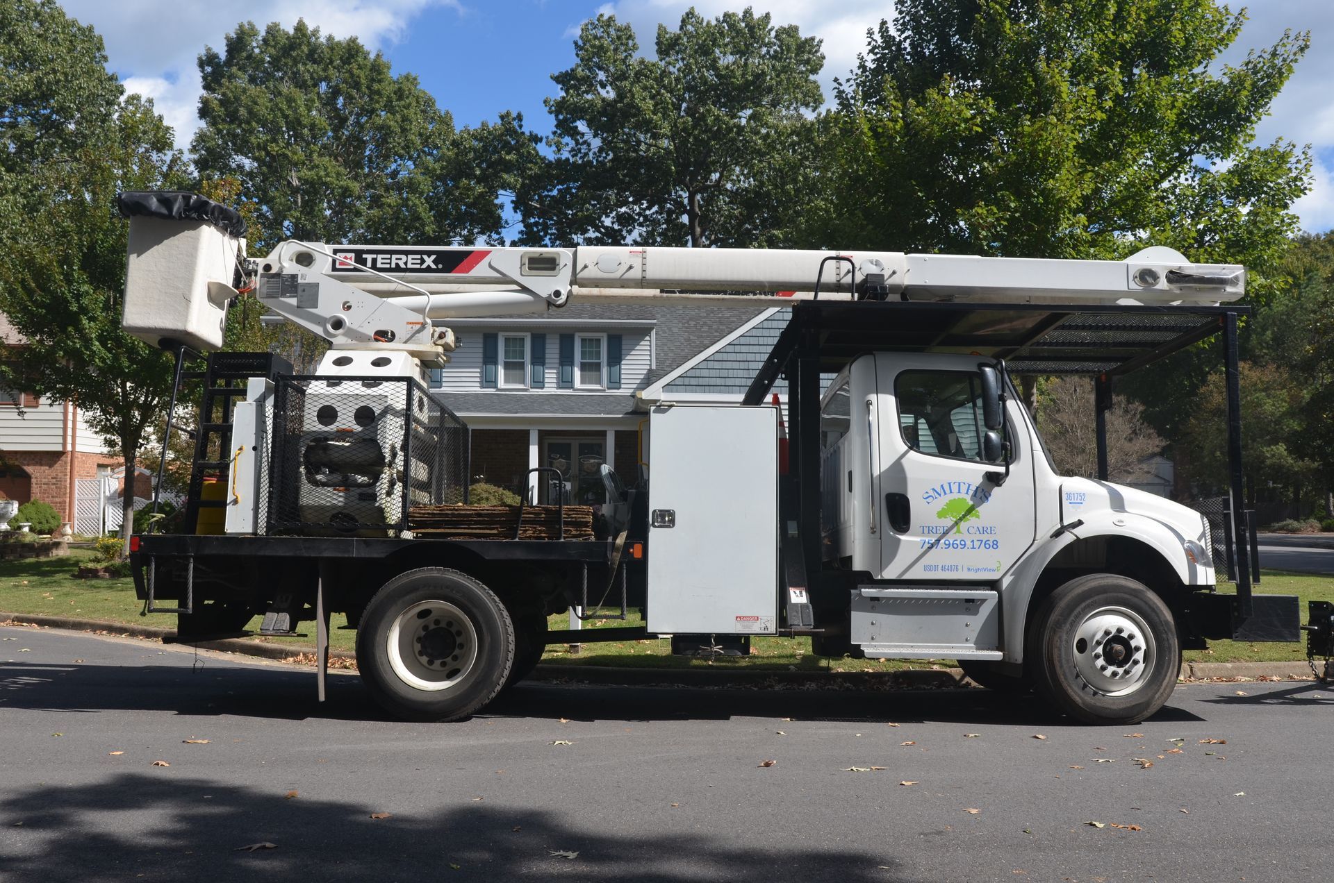 White utility bucket truck parked on a residential street with trees and houses in the background