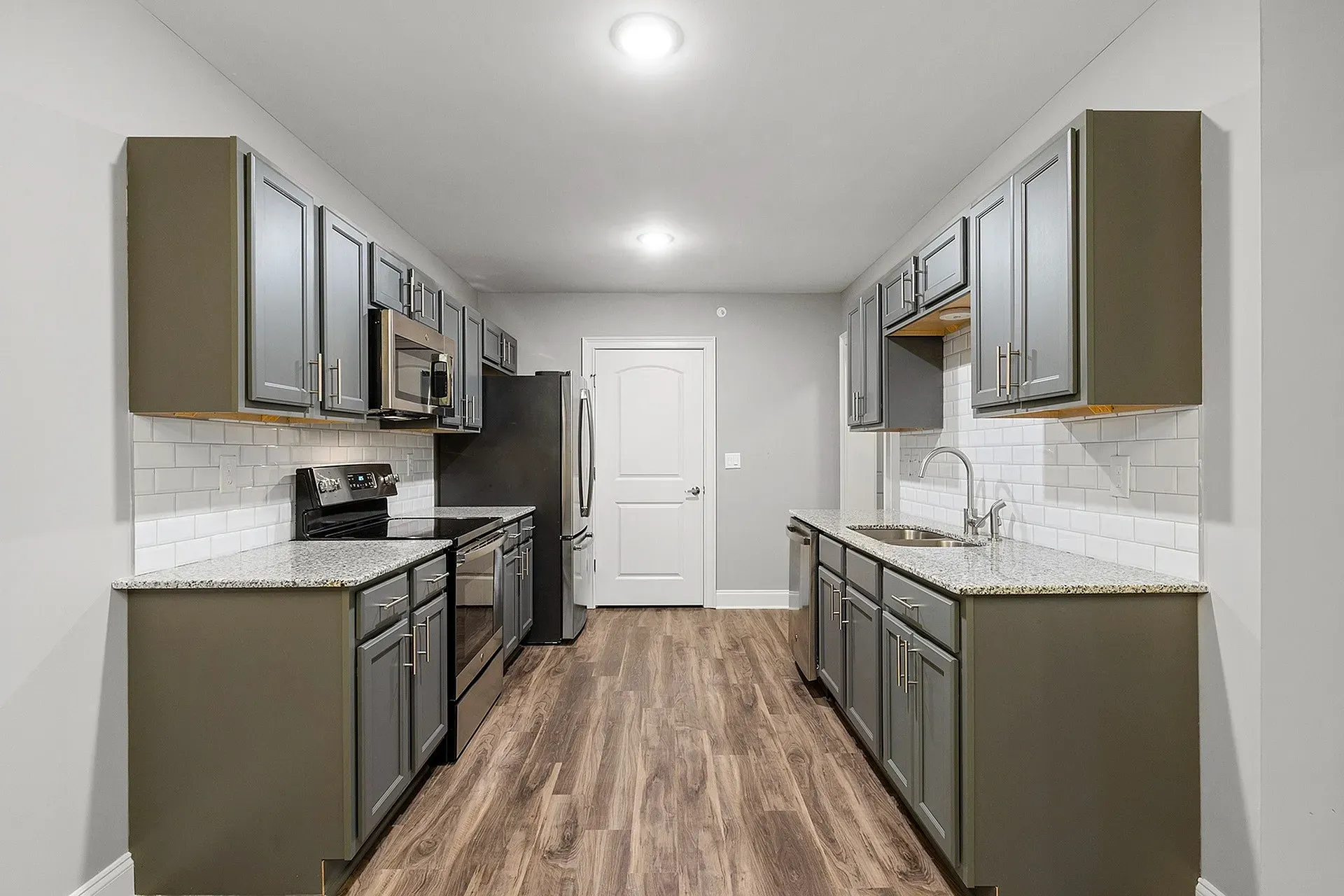 Galley-style kitchen with gray cabinets, stainless-steel appliances, white subway tile, and granite countertops.