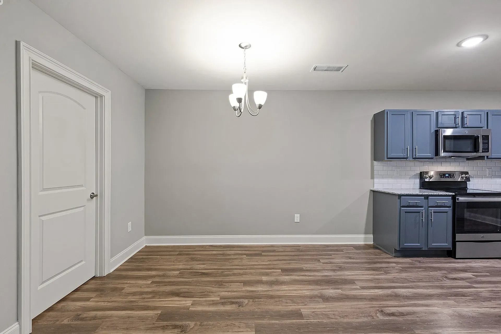 Open-concept kitchen in an apartment with blue cabinets, stainless steel appliances, and wood-look flooring.