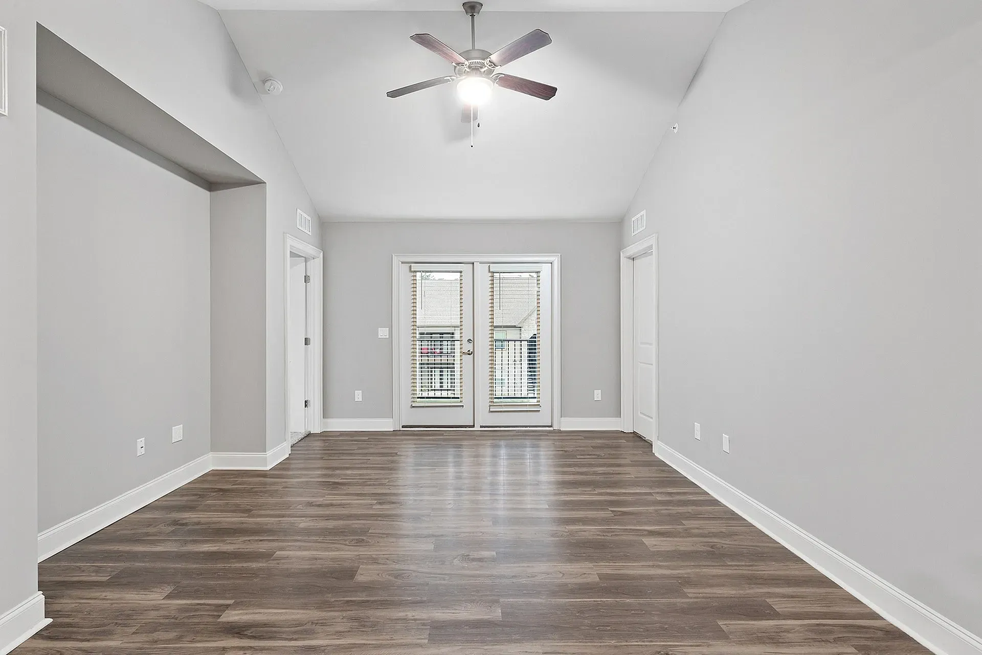 Empty living room with gray walls, wood-look flooring, a ceiling fan, and French doors to a balcony.