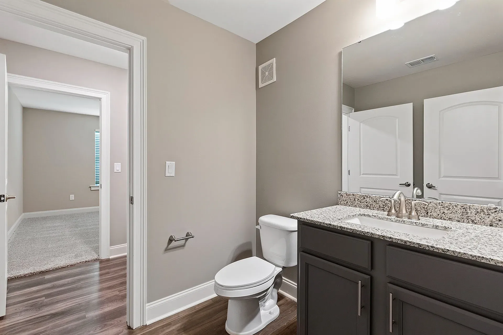 Modern apartment bathroom with granite vanity, single sink, and large mirror.