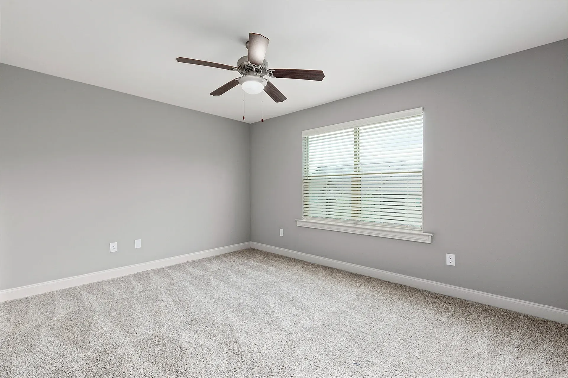 Empty apartment living room with gray walls, carpet, ceiling fan, and window with blinds.