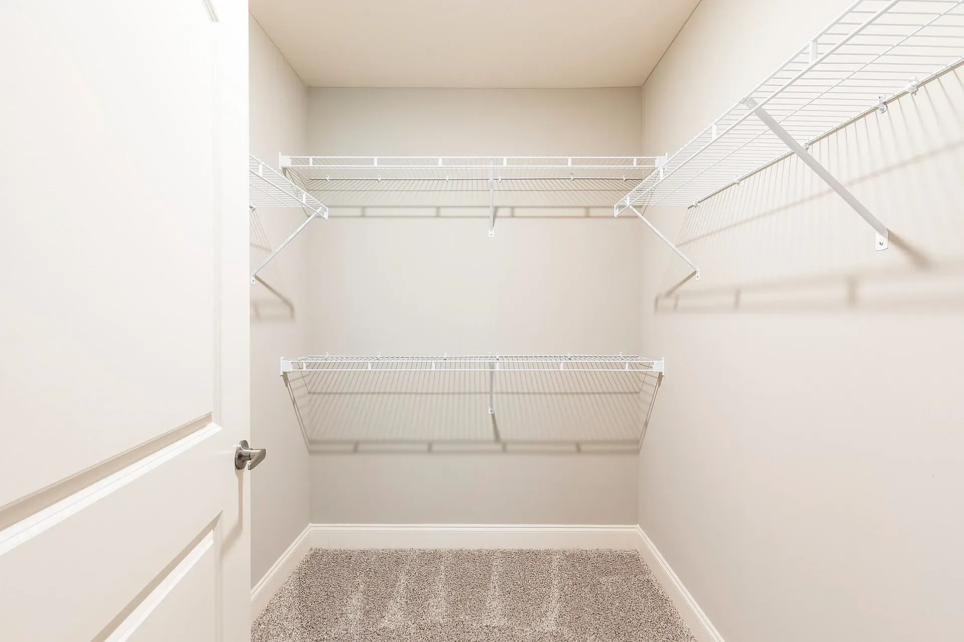 Empty walk-in closet with white wire shelves and beige walls.