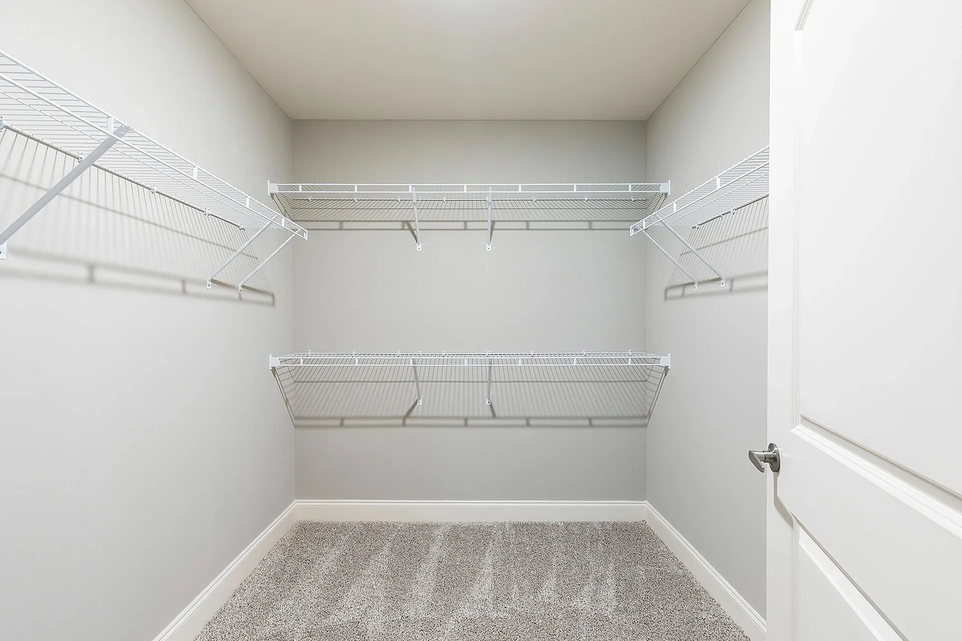 Empty walk-in closet with white wire shelving on both sides.
