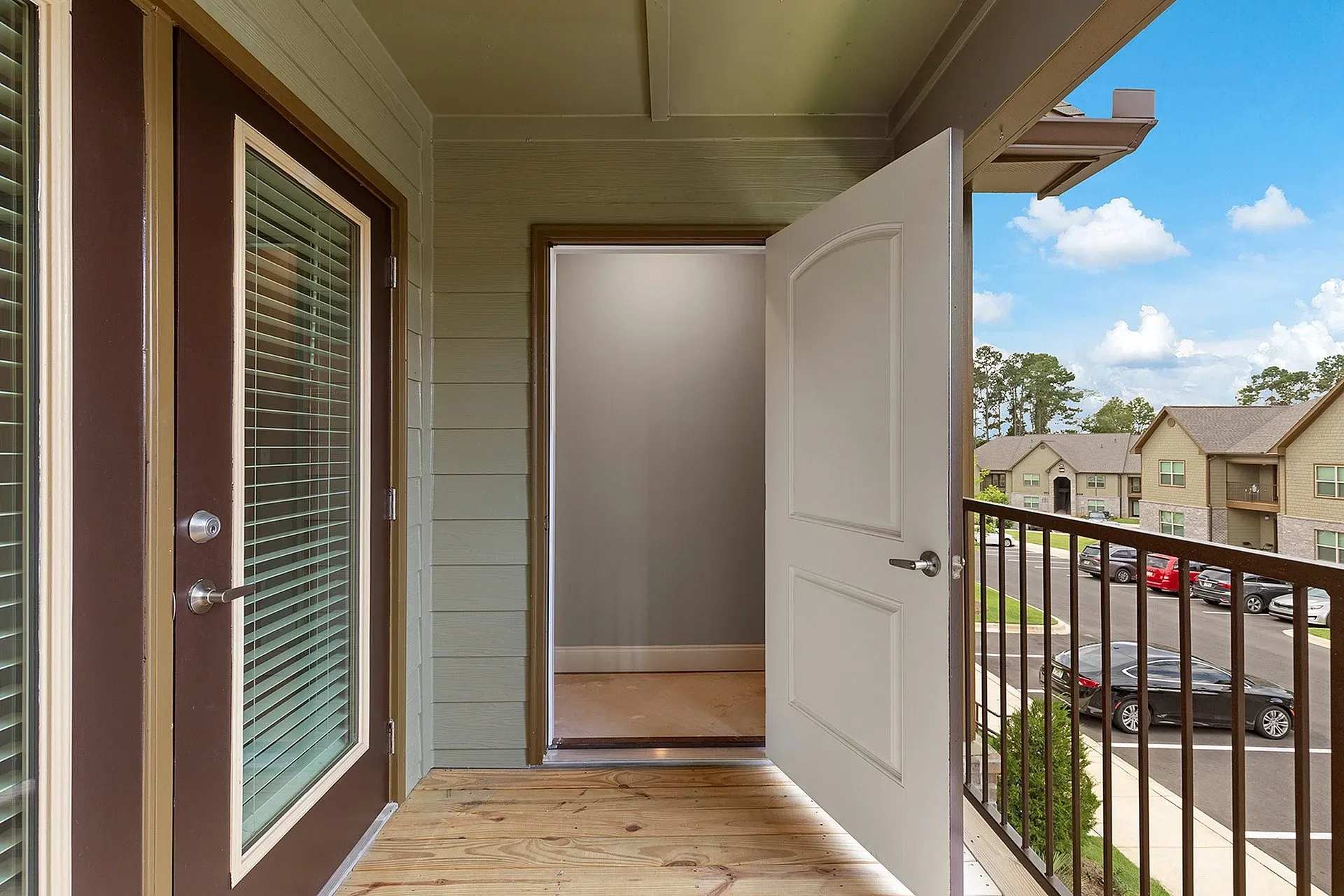 Open balcony door with a small deck railing and a view of nearby buildings and parked cars.