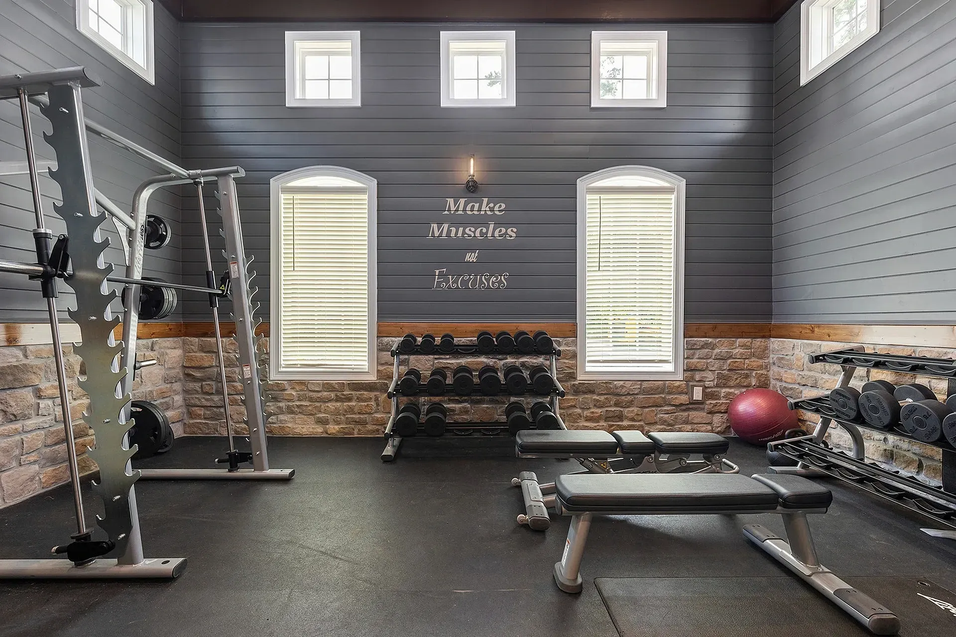 Indoor gym featuring a weight rack, dumbbells, benches, and stone wall accents.