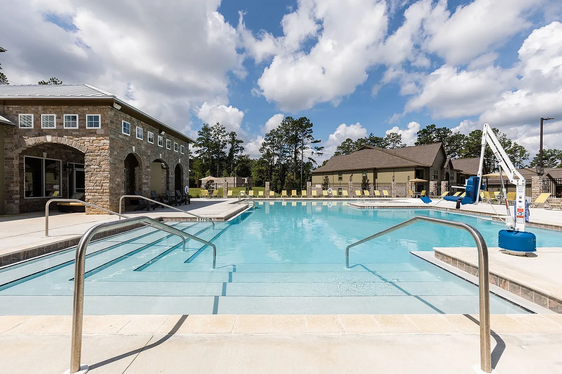 Outdoor community pool with steps, handrails, loungers, and a stone clubhouse.