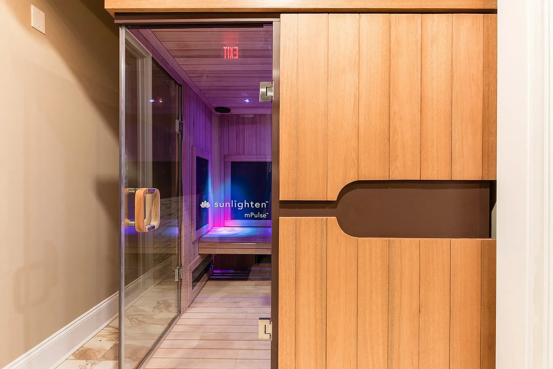 Glass entry to a wood-paneled communal sauna with Sunlighten branding.