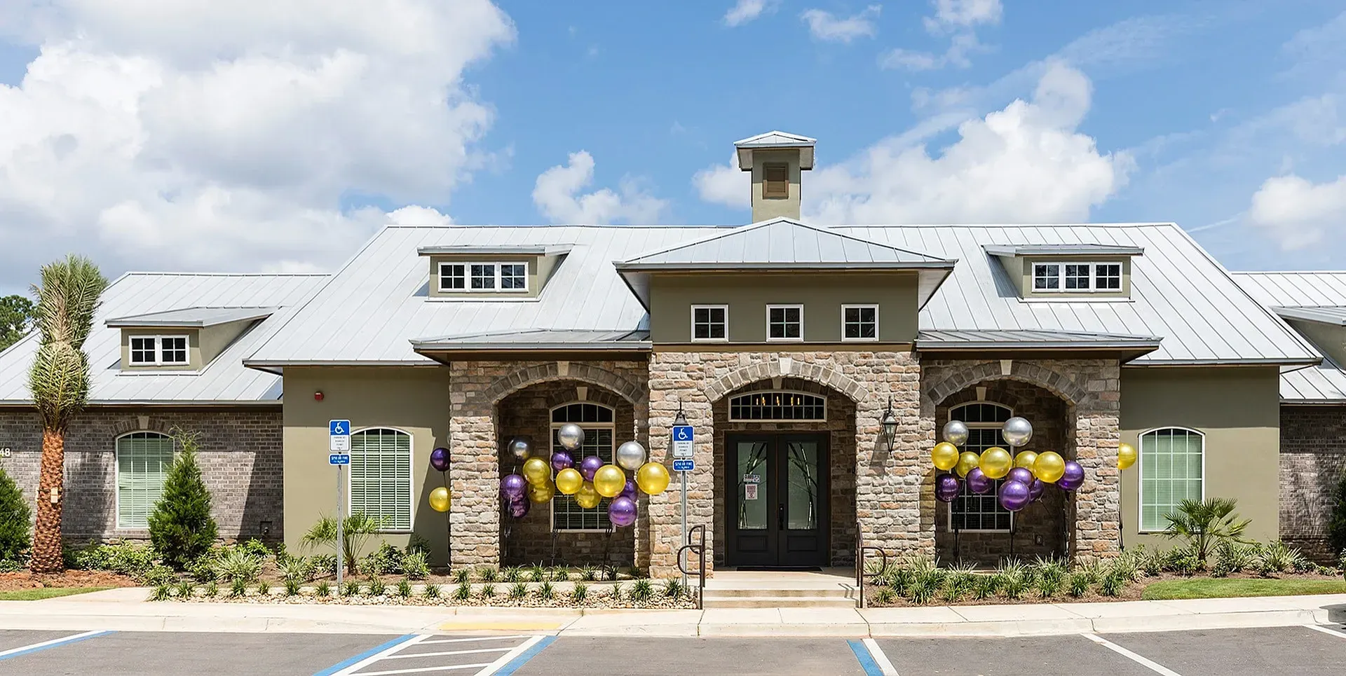 Front view of a stone-clad apartment community entrance with balloons.